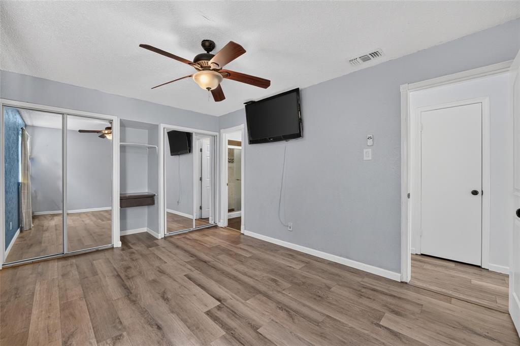 Wood-finish flooring, dual sliding mirrored closet doors, built-in shelving, and a ceiling fan with integrated light fixture