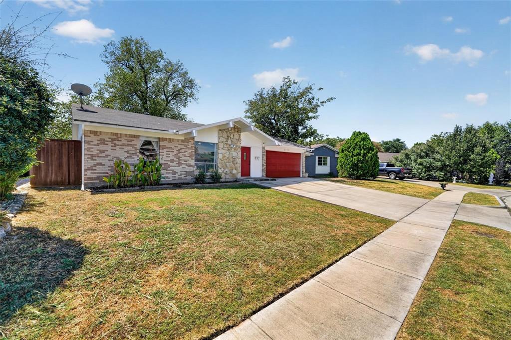 Single-story exterior featuring a brick and stone facade, a concrete driveway, a prominent red front door, and a wood privacy fence Single-story exterior featuring a brick and stone facade, a concrete driveway, a prominent red front door, and a wood privacy fence