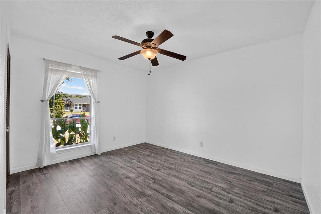 Wood-finish flooring, central ceiling fan with integrated light fixture, and a large window featuring neutral walls