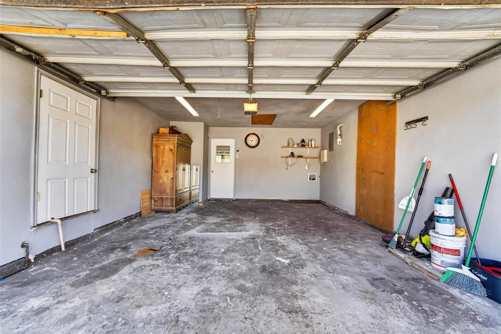 Multi-vehicle garage featuring a paneled sectional door, dual wall-mounted linear light fixtures, two entry doors, and built-in wall shelving