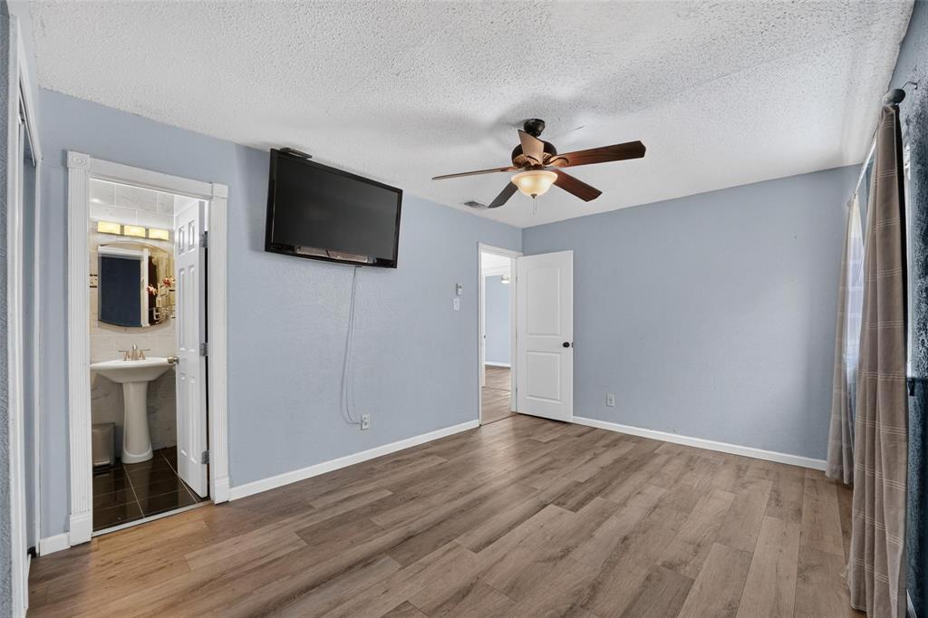 Room featuring wood-finish flooring, a ceiling fan with integrated lighting, and a doorway revealing a pedestal sink