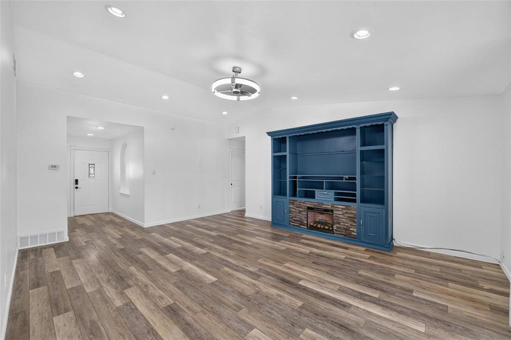 Wood-finish flooring, recessed lighting, ceiling fan with integrated lighting, and custom floor-to-ceiling built-in cabinetry with a stone-finish fireplace surround Wood-finish flooring, recessed lighting, ceiling fan with integrated lighting, and custom floor-to-ceiling built-in cabinetry with a stone-finish fireplace surround