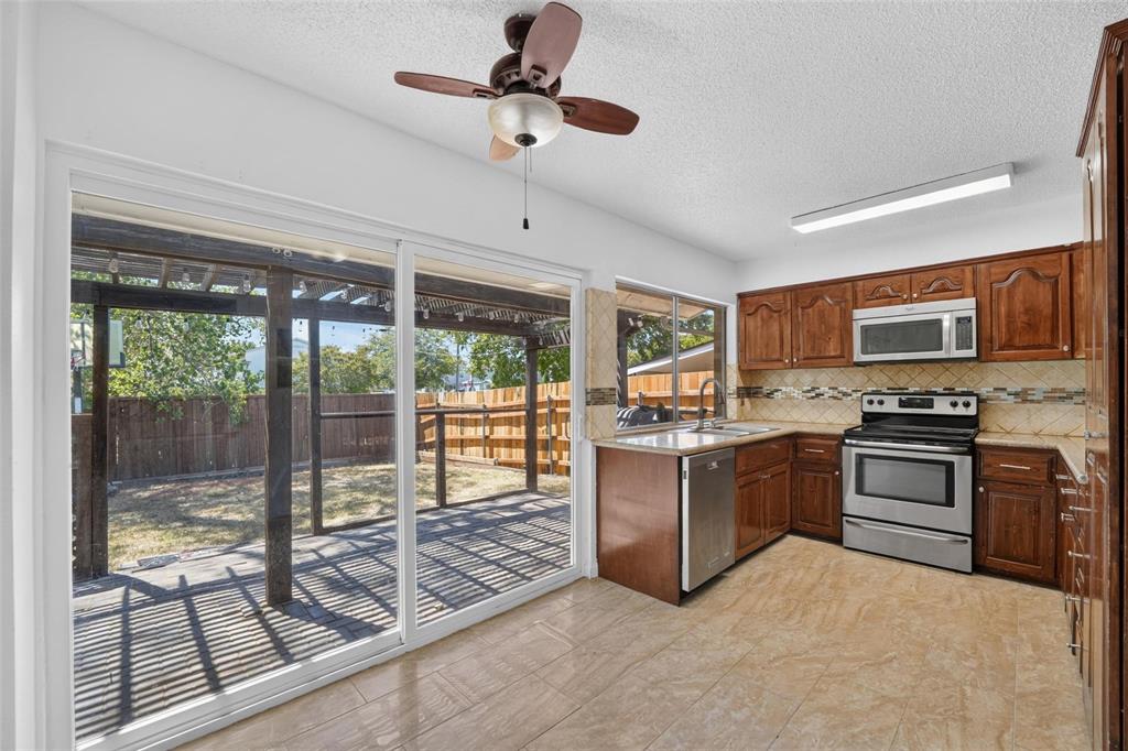 Kitchen featuring stained wood cabinetry, stainless steel appliances, tile flooring, and sliding glass doors opening to a covered patio