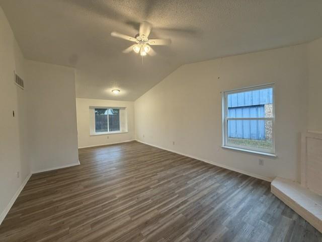 Interior space featuring vaulted ceilings, wood-finish flooring, a ceiling fan with light kit, double-pane windows, and a raised hearth fireplace Interior space featuring vaulted ceilings, wood-finish flooring, a ceiling fan with light kit, double-pane windows, and a raised hearth fireplace