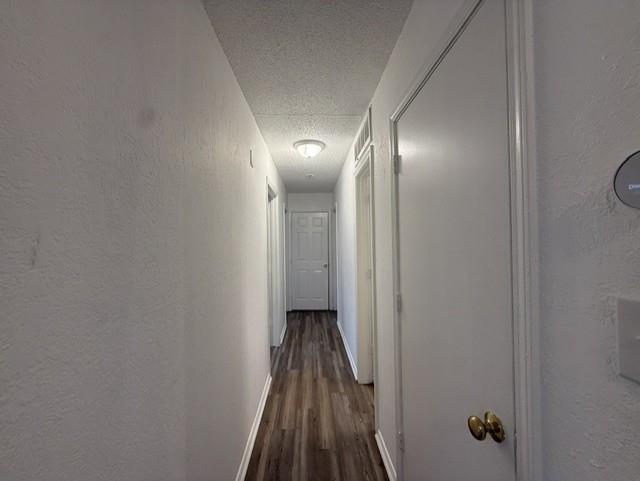Interior hallway featuring wood-finish flooring, textured ceiling, flush-mount lighting, and multiple interior panel doors Interior hallway featuring wood-finish flooring, textured ceiling, flush-mount lighting, and multiple interior panel doors