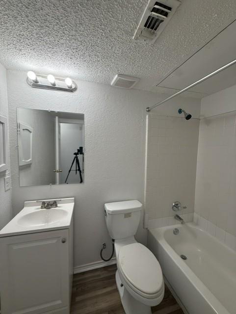 Bathroom featuring a white vanity cabinet with a integrated sink, three-bulb vanity lighting, a wall-mounted mirror, wood-finish flooring, and a tub with tiled surround Bathroom featuring a white vanity cabinet with a integrated sink, three-bulb vanity lighting, a wall-mounted mirror, wood-finish flooring, and a tub with tiled surround