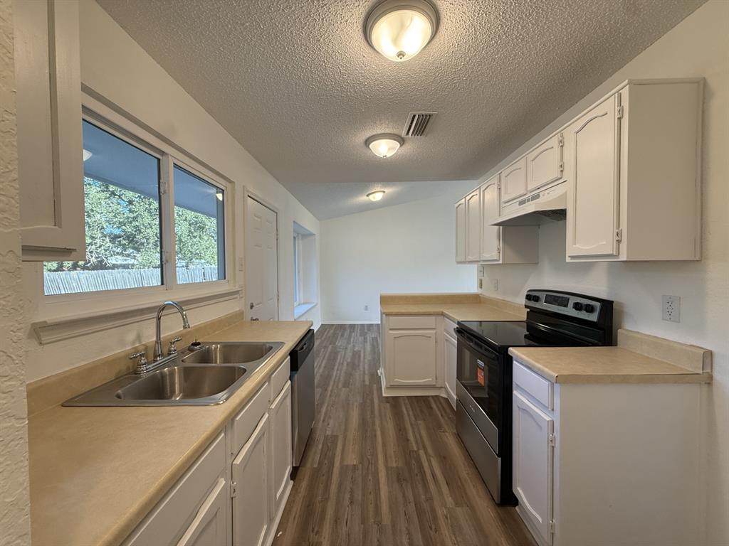 Kitchen featuring white cabinetry, wood-finish flooring, dual-basin stainless steel sink, and a range with overhead range hood Kitchen featuring white cabinetry, wood-finish flooring, dual-basin stainless steel sink, and a range with overhead range hood