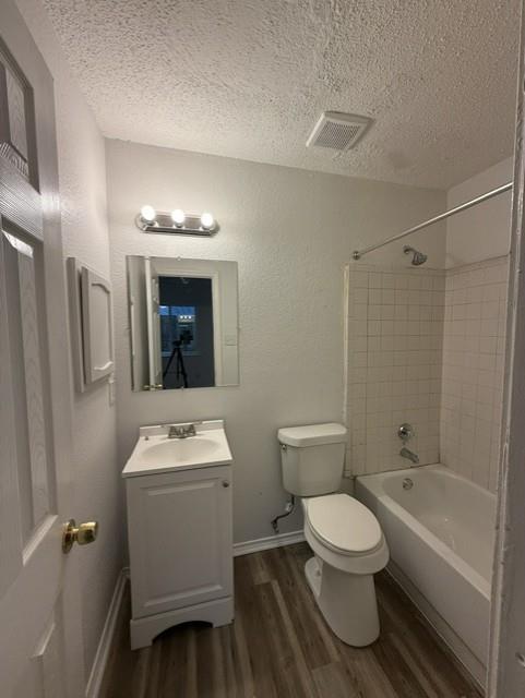 Bathroom featuring a vanity with an integrated sink, wood-finish flooring, a wall-mounted vanity light fixture, and a tile-surround shower and tub combination