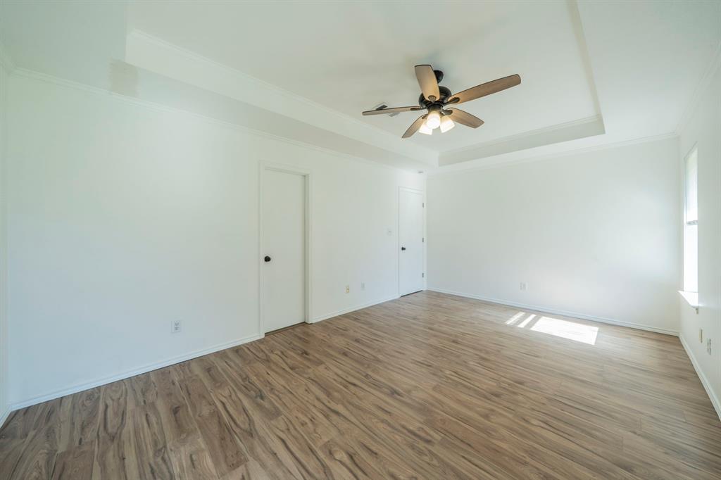 Primary b-room Tray ceiling featuring a central multi-blade ceiling fan with integrated lighting and wood-finish flooring