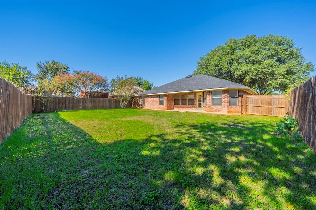 Rear exterior featuring a brick facade, hip roof, wood privacy fencing, and expansive green lawn