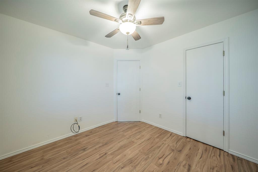 Neutral interior featuring wood-finish flooring, a ceiling fan with integrated lighting, and two interior doors with matte black hardware