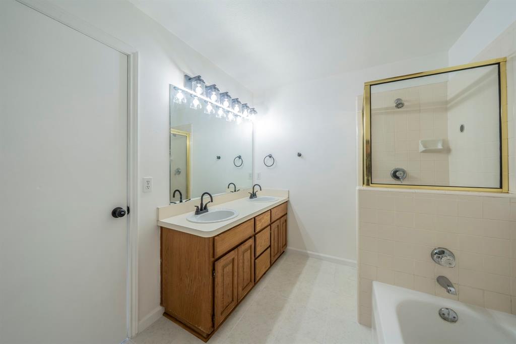Double vanity featuring wood-finish cabinetry, dual undermount sinks, matte black fixtures, and an expansive wall mirror with a multi-bulb light fixture