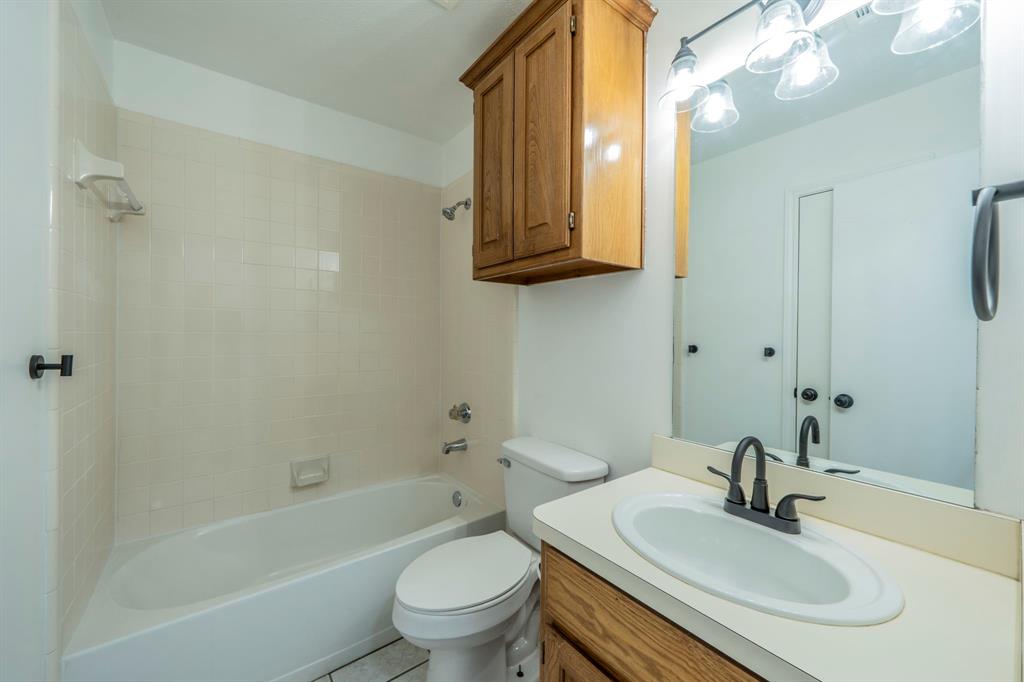 Bathroom featuring a tub-shower combination with tiled surround, wood-finish wall cabinet, vanity with integrated basin, matte black hardware, and overhead multi-light fixture