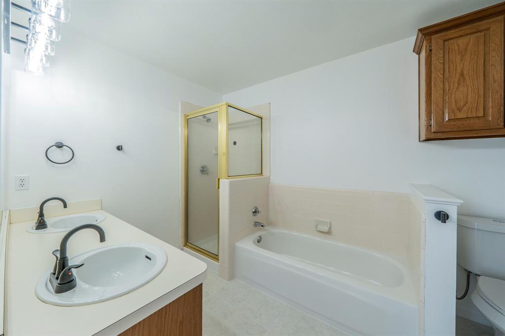 Dual-sink vanity with matte black faucets, glass-enclosed shower, tiled soaking tub, and wall-mounted wooden cabinetry