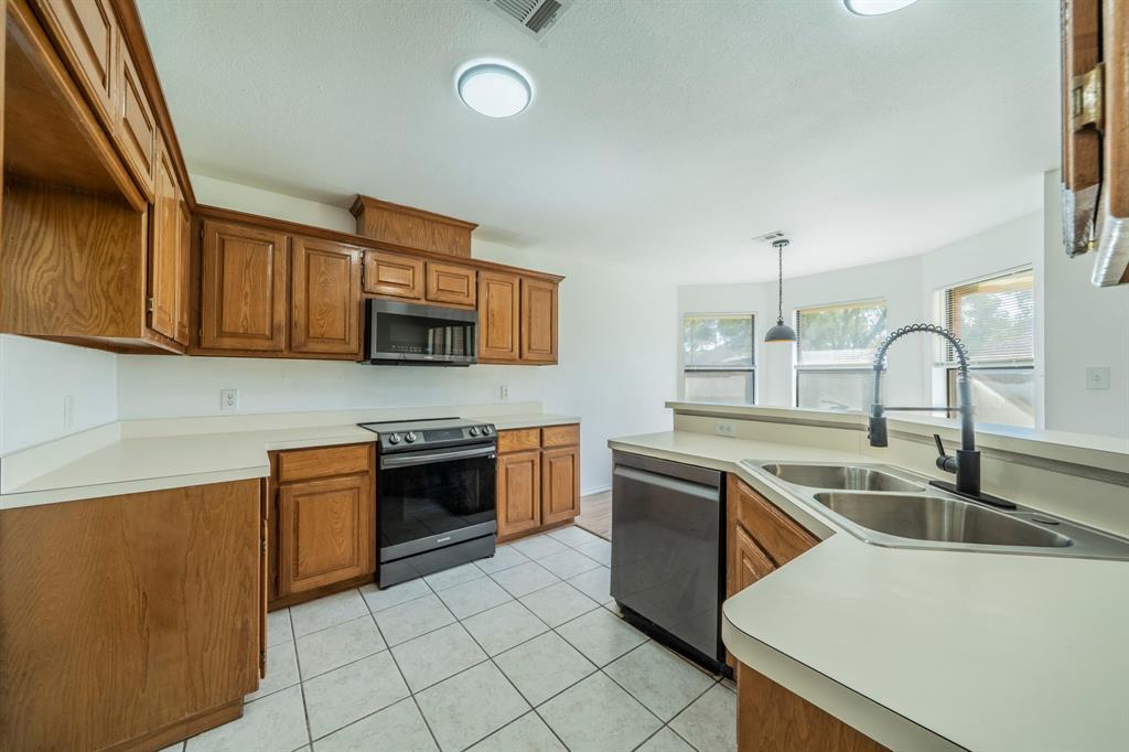 Kitchen featuring wood cabinetry, stainless steel appliances, solid surface countertops, a stainless steel double-basin sink with a matte black pull-down faucet, and tiled flooring