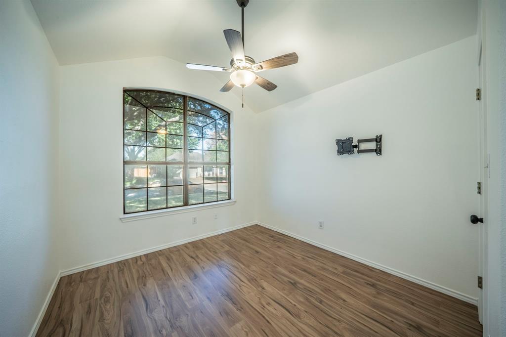 Vaulted ceiling room featuring wood-finish flooring, a multi-pane arched window, and a central ceiling fan with an integrated light fixture