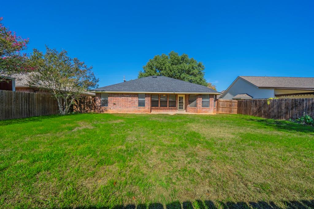 Expansive backyard featuring a large grass lawn, brick exterior, wood privacy fencing, and mature trees