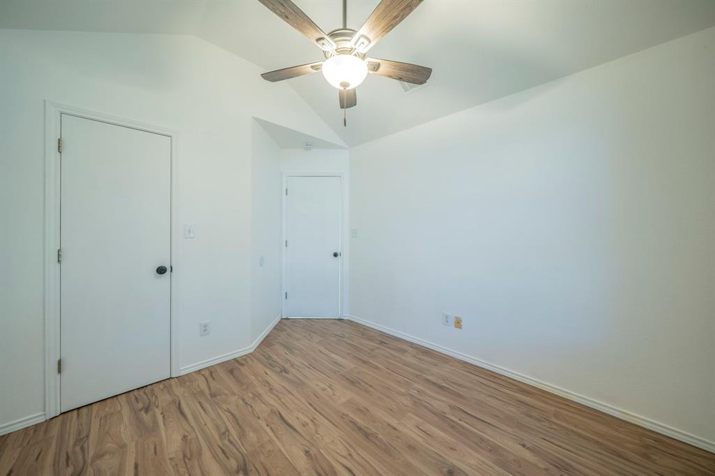 Vaulted ceiling featuring a central ceiling fan with wood-finish blades and integrated lighting, complemented by wood-finish flooring and solid-core interior doors