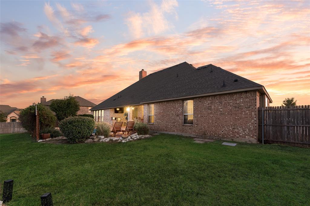 Brick exterior residence featuring a covered patio, rock-lined landscaping, a fenced backyard, and a shingle roof