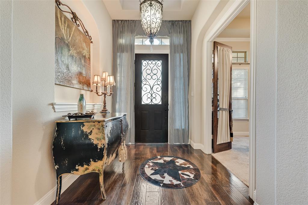 Foyer featuring wood-finish flooring, an arched entryway, recessed ceiling detailing, an ornate hanging pendant light, and a front door with decorative iron scrollwork