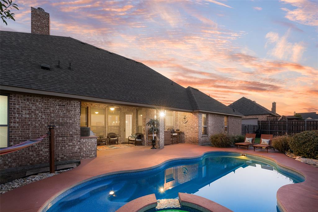 Brick exterior residence featuring a rear swimming pool with integrated spa, expansive stained concrete patio, and a covered outdoor living area