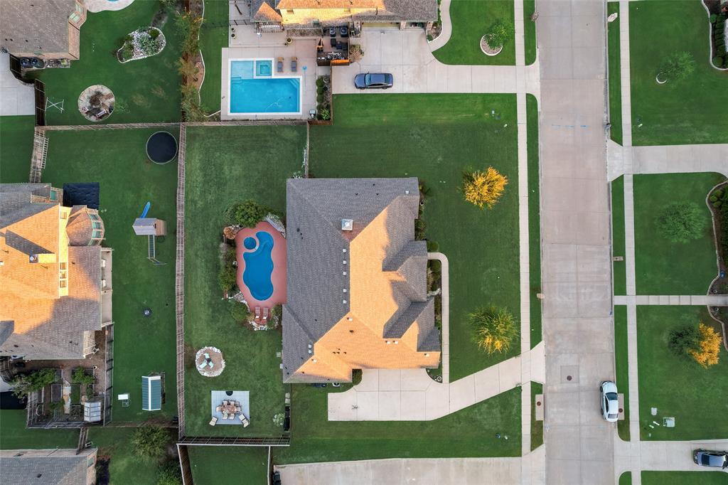 Aerial perspective of a property featuring an in-ground swimming pool with an integrated spa, expansive lawn, concrete driveway, and wood fencing