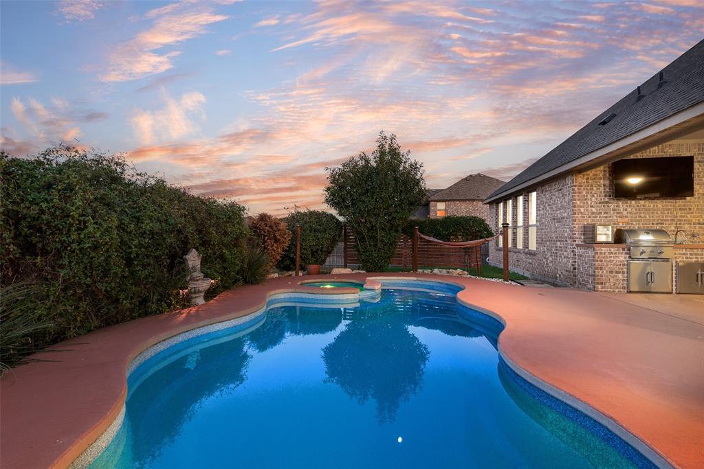 Outdoor living space featuring an inground pool with an integrated spa, a brick exterior wall, and a built-in stainless steel outdoor kitchen