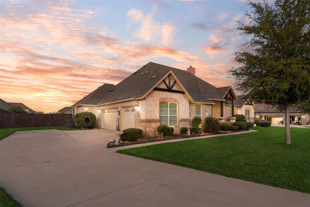 Single-story brick and stone veneer exterior featuring a multi-gable roofline, attached two-car garage, expansive concrete driveway, and manicured landscaping