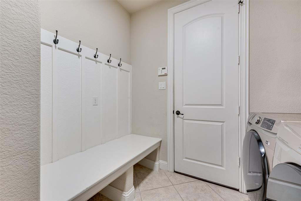Built-in white board-and-batten mudroom bench featuring black hardware hooks, arched-top interior door, and ceramic tile flooring
