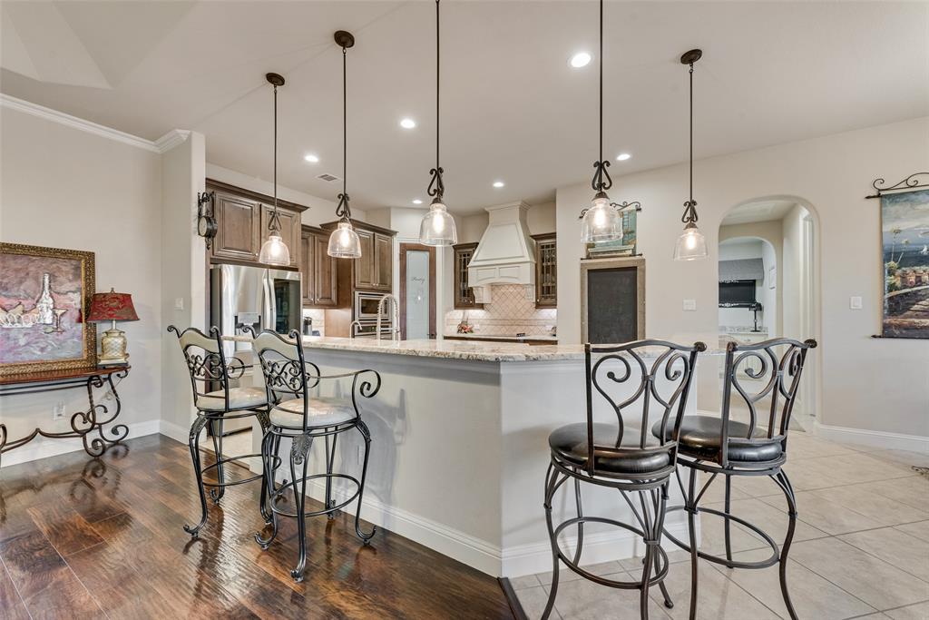 Kitchen featuring a tiered stone-surface island, wood-finish cabinetry, a decorative stove hood, recessed lighting, and glass pendant fixtures