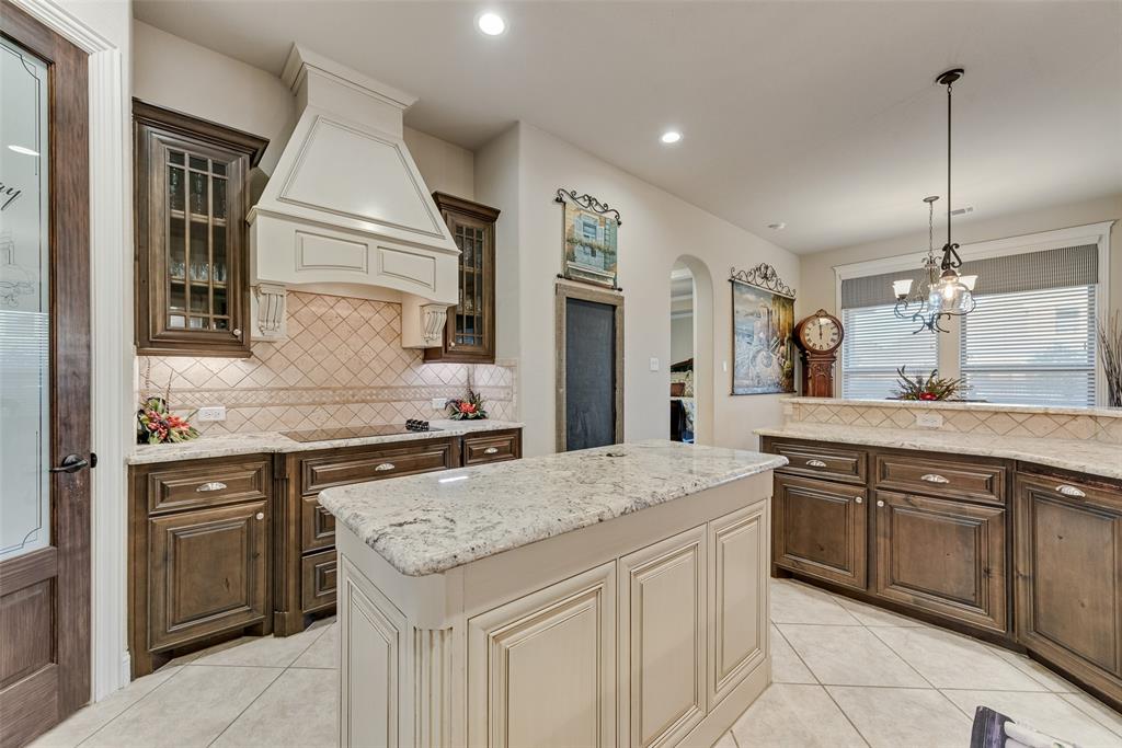 Kitchen featuring custom wood cabinetry, stone countertops, central island, tiled backsplash, and decorative range hood