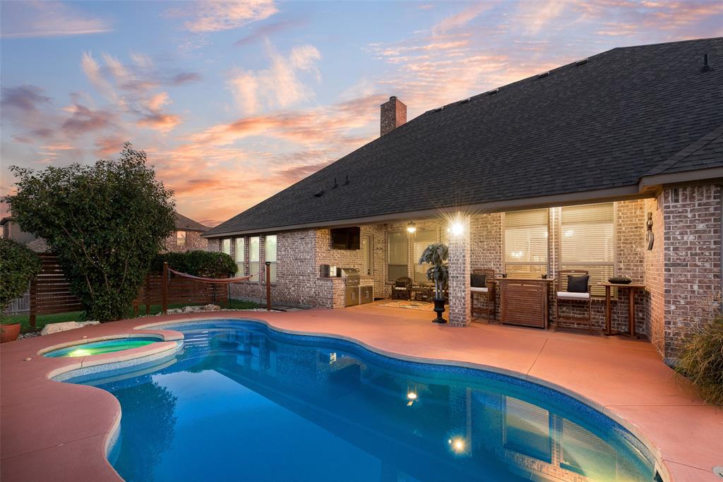 Brick exterior, covered patio, and in-ground swimming pool with an attached spa, complemented by an outdoor kitchen station