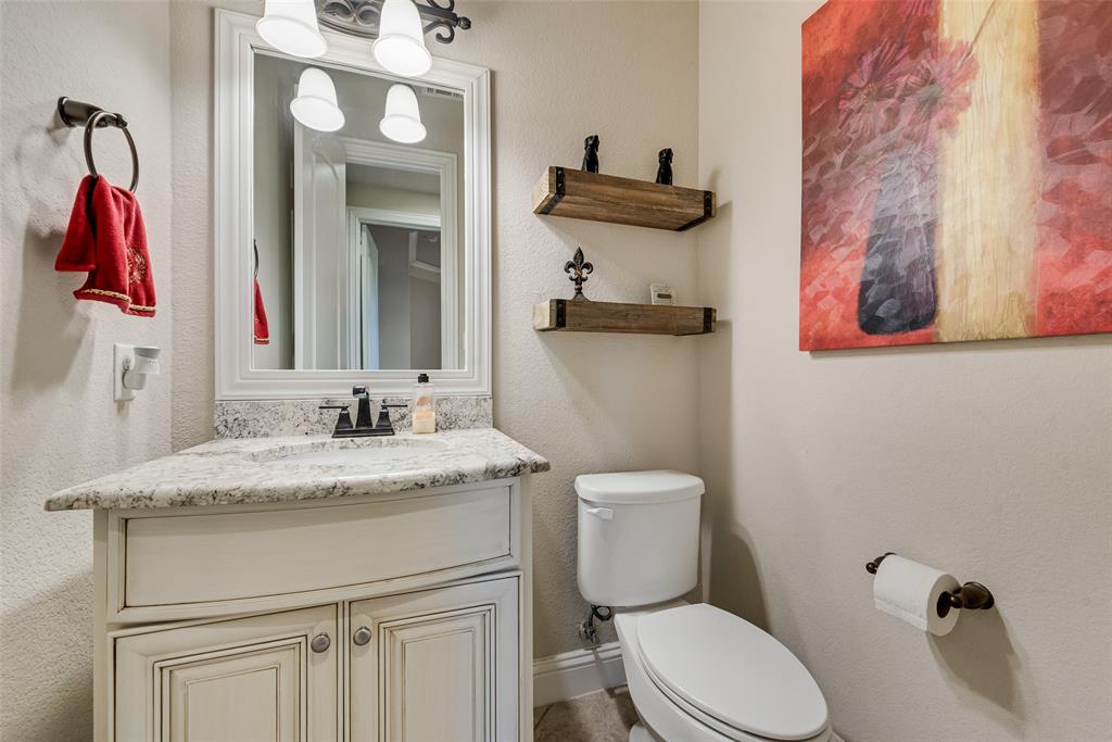 Curved cabinetry with stone countertop, undermount sink, multi-light fixture, framed wall mirror, and floating wood shelving