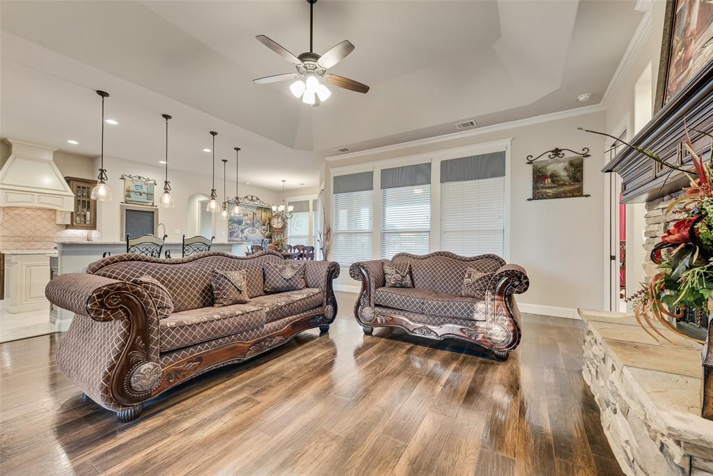 Tray ceiling with integrated fan, wood-finish flooring, stone-surround fireplace with mantel, and recessed lighting