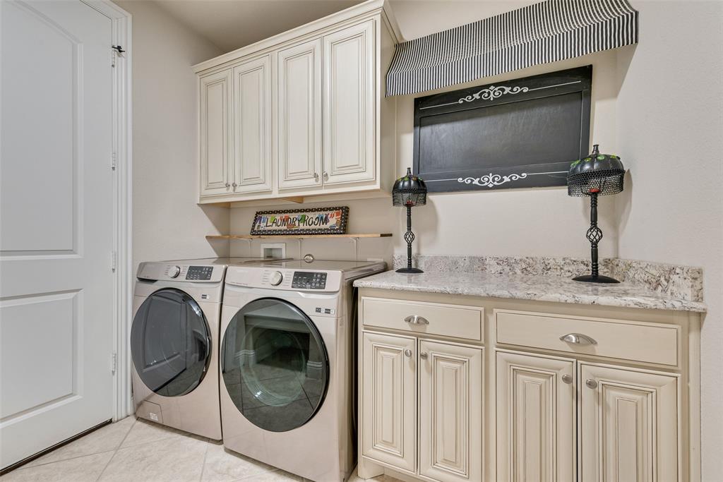 Laundry area featuring raised-panel cabinetry, light-toned stone-patterned countertops, and tile flooring