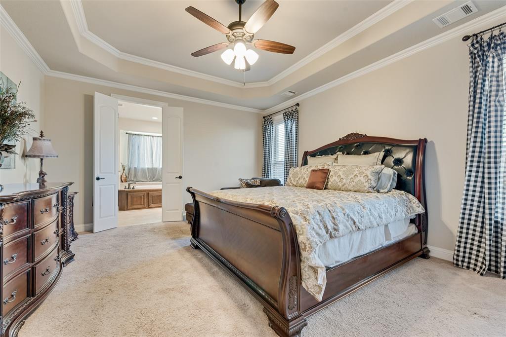 Tray ceiling with crown molding, plush carpeting, and a multi-blade ceiling fan with integrated lighting