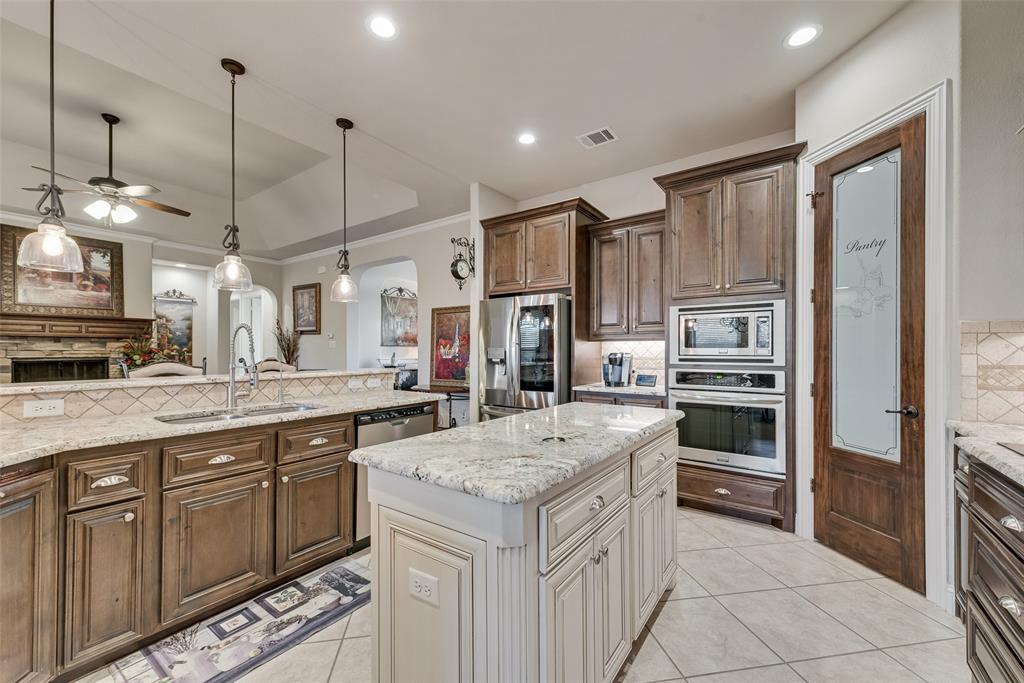 Kitchen featuring stained wood cabinetry, stone-finish countertops, a center island with a contrasting finish, stainless steel built-in double wall ovens, and a pantry door with decorative glass paneling
