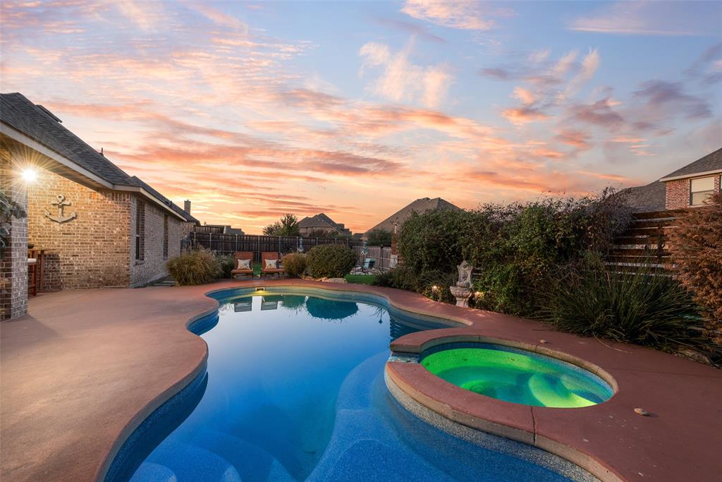 Curved swimming pool with an integrated spa, set within a stamped concrete patio and enclosed by a brick exterior wall