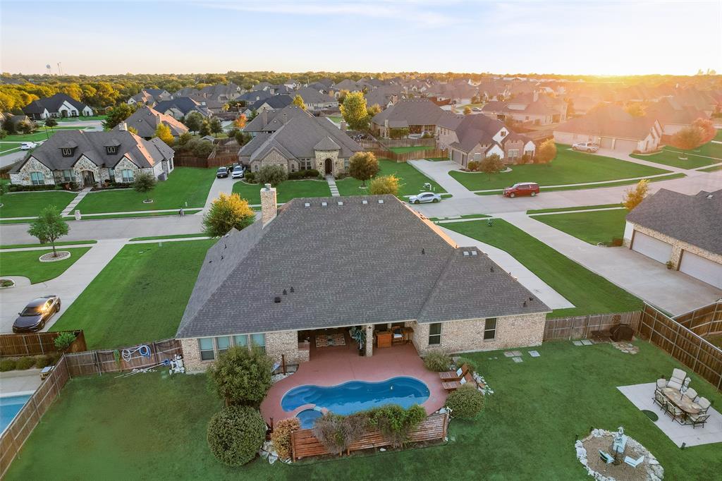 Aerial view of brick exterior residence featuring a covered patio, swimming pool with integrated spa, manicured lawn, and wood privacy fencing
