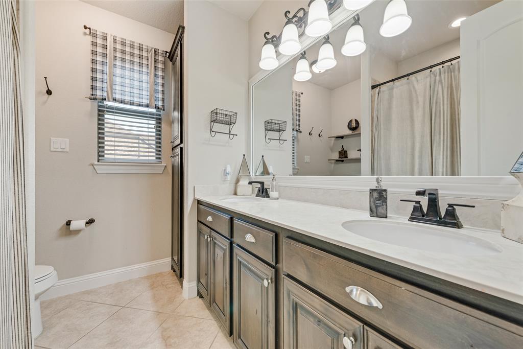 Dual-sink vanity featuring stone-finish countertops, dark-stained cabinetry with recessed-panel doors, matte black fixtures, and a large framed wall mirror