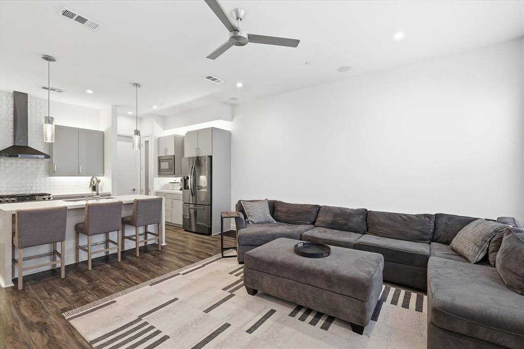 Kitchen featuring a quartz-topped island, stainless steel appliances, flat-panel cabinetry, a stainless steel range hood, and wood-finish flooring