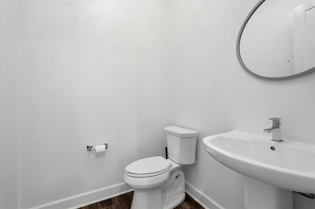 Pedestal sink with a single-handle faucet, oval wall-mounted mirror with a metallic frame, and wood-finish flooring