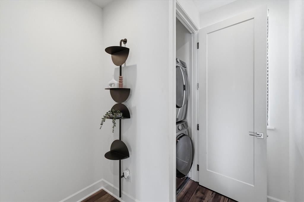 Dedicated laundry area featuring a stacked washer and dryer, wood-finish flooring, and a solid-core interior door with modern lever hardware