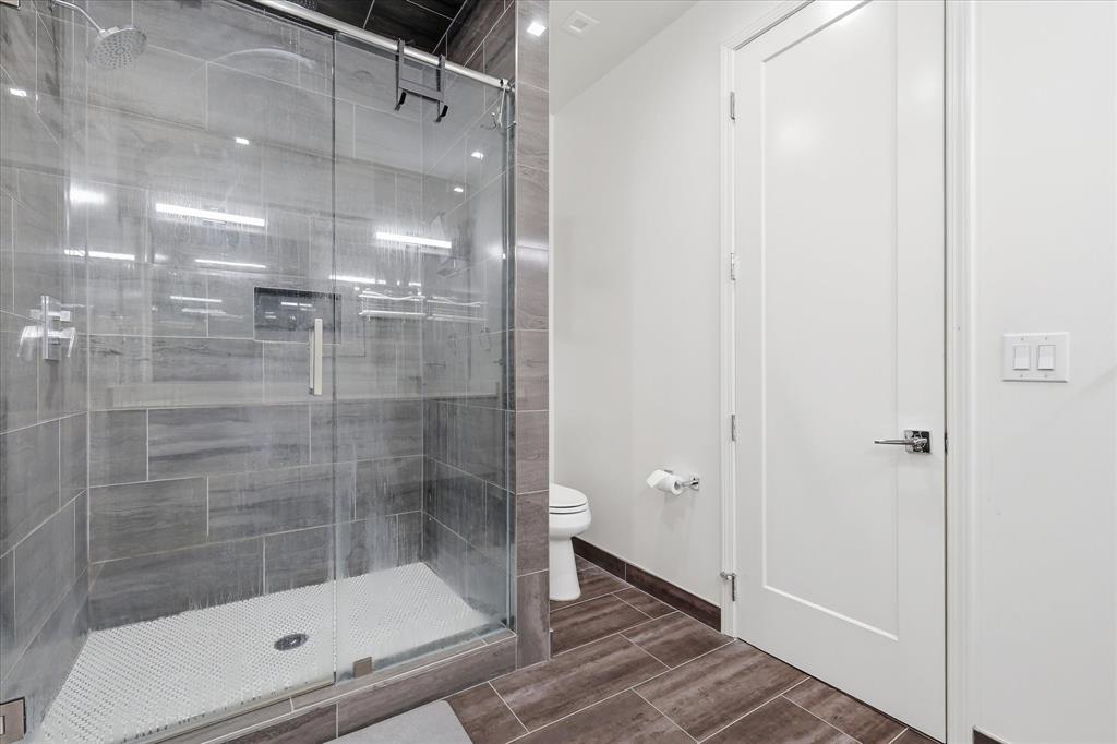 Walk-in shower featuring glass enclosure, large-format grey wall tile, built-in recessed wall niche, and textured tile floor, complemented by wood-finish floor tiling