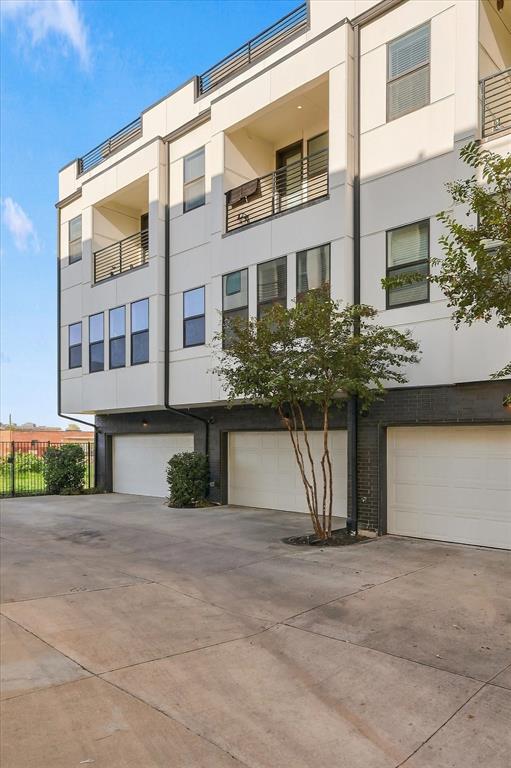 Modern multi-story exterior featuring a white panel facade, dark brick lower level, private balconies with metal railings, and three individual garage bays