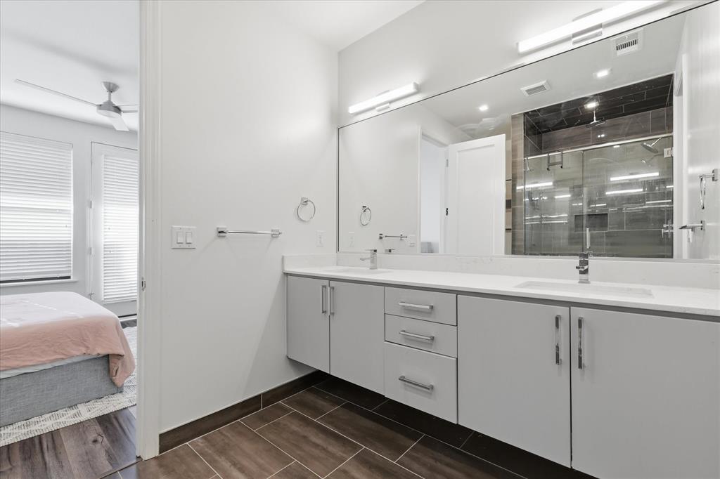 Floating double vanity with a stone countertop, dual undermount sinks, full-width vanity mirror, and wood-finish flooring