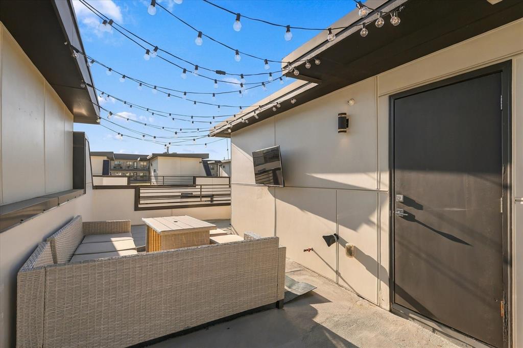 Rooftop terrace featuring concrete flooring, overhead string lighting, a wall-mounted television, and metal railing