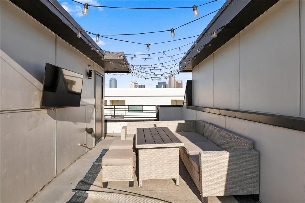 Rooftop terrace featuring concrete flooring, perimeter wall-mounted string lighting, metal railing, and city skyline backdrop