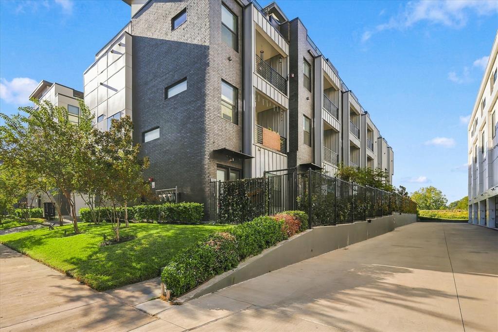 Modern multi-story exterior featuring dark brick masonry, vertical metal siding, recessed balconies with metal railings, and a tiered landscaped border