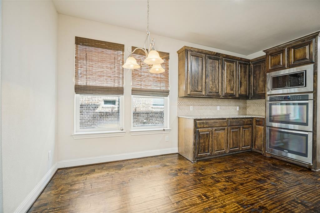 Stained wood cabinetry, built-in stainless steel double wall oven and microwave, granite countertops, wood-finish flooring, and multi-light chandelier